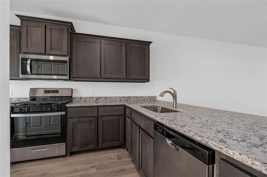 Kitchen featuring appliances with stainless steel finishes, light stone counters, and dark brown cabinetry