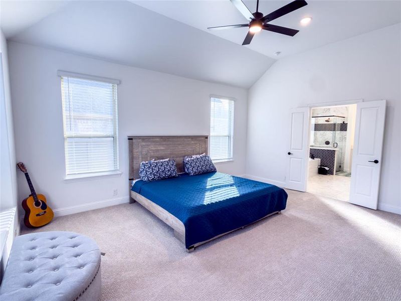 Carpeted bedroom featuring lofted ceiling, ensuite bathroom, and a ceiling fan