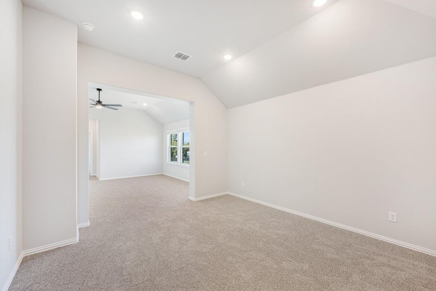 Empty bedroom with vaulted ceiling, carpet flooring, and open doorway to adjoining room with ceiling fan Empty bedroom with vaulted ceiling, carpet flooring, and open doorway to adjoining room with ceiling fan