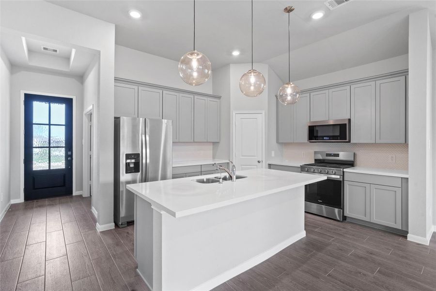 Discover this chef-ready kitchen featuring sleek, shaker-style grey cabinetry, Frost White quartz countertops, and a full suite of stainless steel appliances, including an over-the-range microwave and a side-by-side refrigerator.
