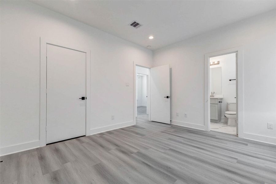 This spacious bedroom combines a clean modern palette with gray-toned plank flooring, recessed lighting, and generous wall space. A private adjoining bathroom adds everyday convenience, while multiple doors provide access to the closet, hallway, and neighboring areas for a comfortable, functional layout. This spacious bedroom combines a clean modern palette with gray-toned plank flooring, recessed lighting, and generous wall space. A private adjoining bathroom adds everyday convenience, while multiple doors provide access to the closet, hallway, and neighboring areas for a comfortable, functional layout.