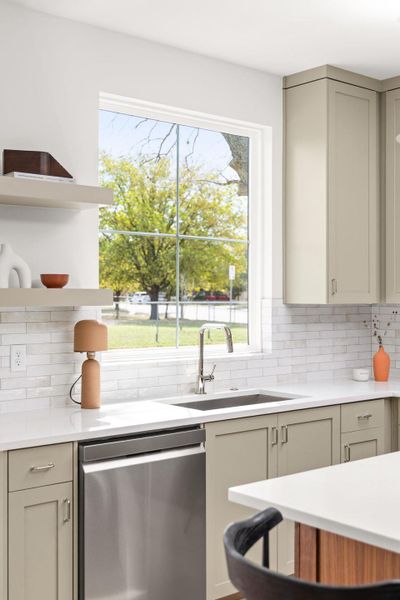Kitchen with open shelves, stainless steel dishwasher, backsplash, light stone countertops, and plenty of natural light