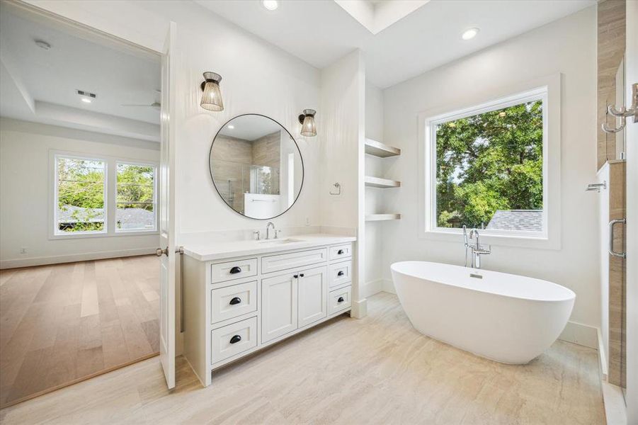 The primary ensuite bath is bathed in natural light from a large picture window, with a freestanding soaking tub perfectly positioned beneath it—an ideal spot for ultimate relaxation.