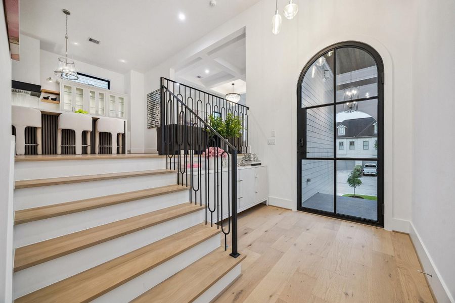Another view of the formal entrance of the home. The space is defined by soaring ceilings and an abundance of natural light streaming in through the large black-framed iron glass door with 6 divided lite windows, creating a bright and welcoming atmosphere.