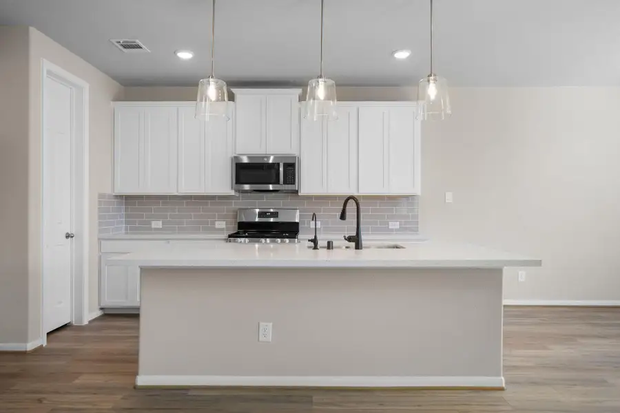 This light and bright kitchen features a large quartz island, white cabinets, a large sink overlooking your family room, recessed lighting, and beautiful backsplash.