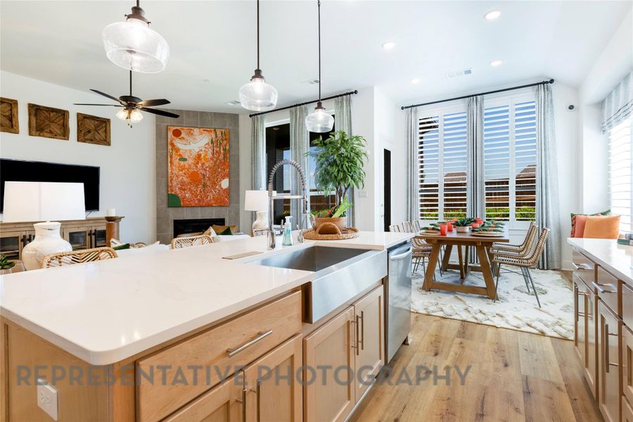 Kitchen with light brown cabinetry, light wood finished floors, pendant lighting, a tiled fireplace, and light stone counters Kitchen with light brown cabinetry, light wood finished floors, pendant lighting, a tiled fireplace, and light stone counters
