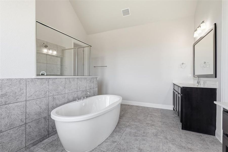 Full bathroom with lofted ceiling, vanity, a stall shower, a freestanding bath, and tile walls Full bathroom with lofted ceiling, vanity, a stall shower, a freestanding bath, and tile walls
