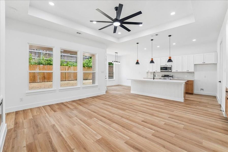 Open-concept living space featuring wood-finish flooring, a tray ceiling with a contemporary ceiling fan, and recessed lighting Open-concept living space featuring wood-finish flooring, a tray ceiling with a contemporary ceiling fan, and recessed lighting