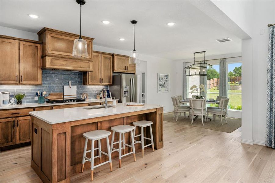 Kitchen featuring an island with sink, black gas cooktop, light wood-type flooring, stainless steel refrigerator with ice dispenser, and sink