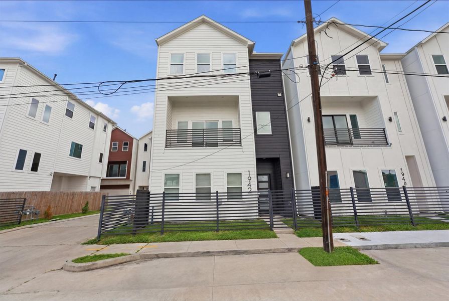 Contemporary three-story townhome with sleek modern exterior, balcony, and fenced front yard in a desirable urban setting.