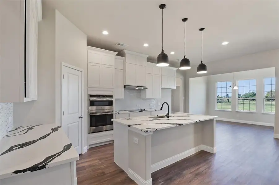 Kitchen with hanging light fixtures, decorative backsplash, an island with sink, double oven, and white cabinetry