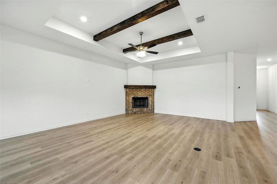 Unfurnished living room featuring light wood-type flooring, a ceiling fan, beam ceiling, a brick fireplace, and recessed lighting