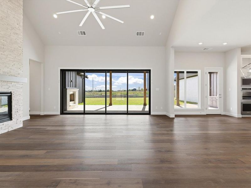 Unfurnished living room featuring high vaulted ceiling, plenty of natural light, dark wood-style floors, recessed lighting, and a fireplace