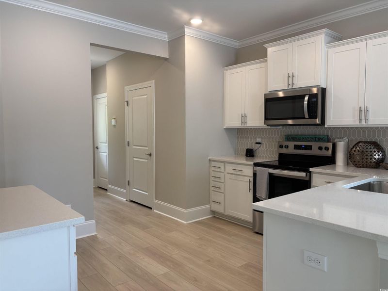 Kitchen with stainless steel appliances, light countertops, white cabinetry, backsplash, and ornamental molding
