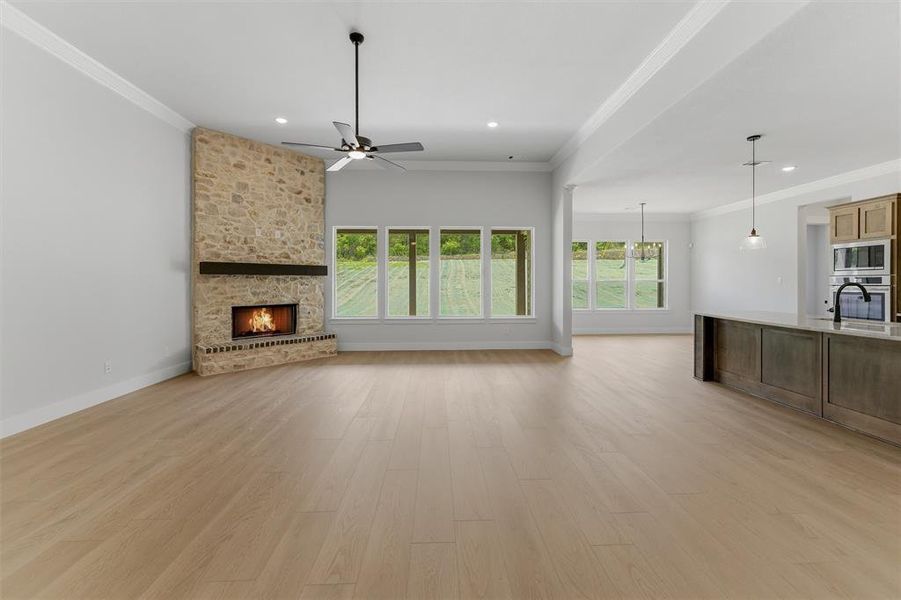 Spacious living area featuring light wood-finish flooring, a stone-clad fireplace with a dark wood mantel, and a ceiling fan