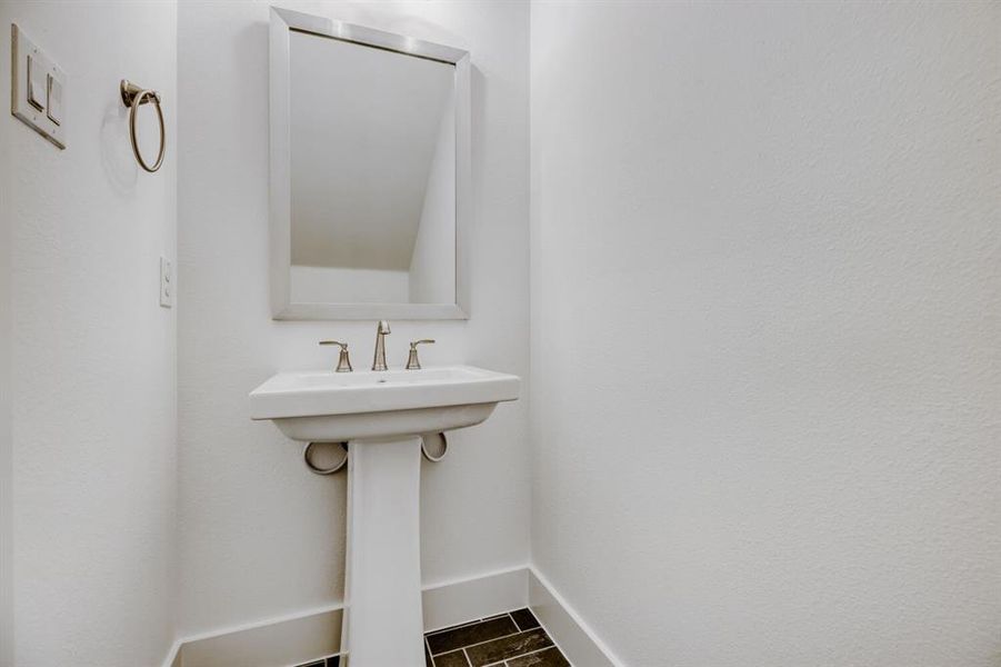 Pedestal sink with brushed nickel faucet, framed mirror, and dark tile flooring