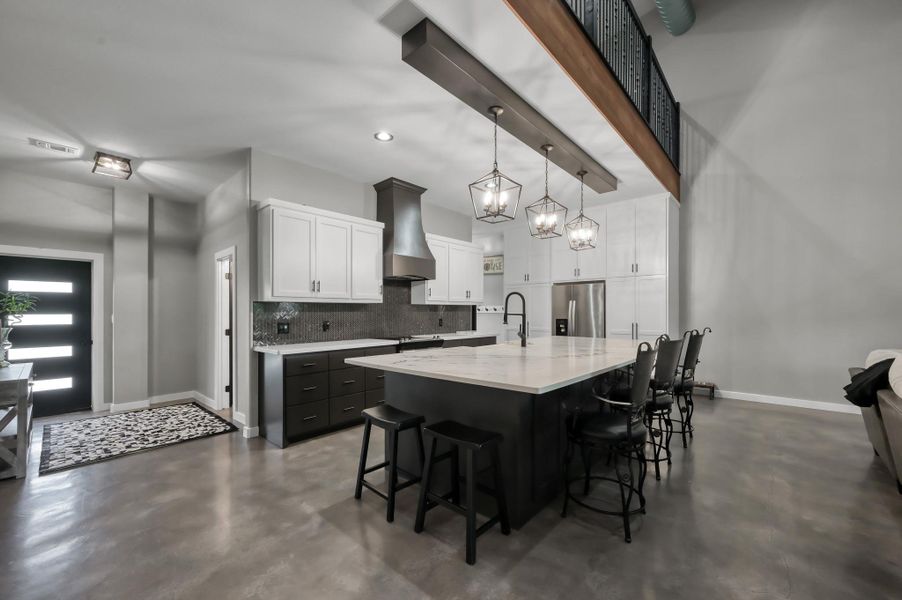 large island with seating, and contemporary lighting. It includes ample white cabinetry, stainless steel appliances,