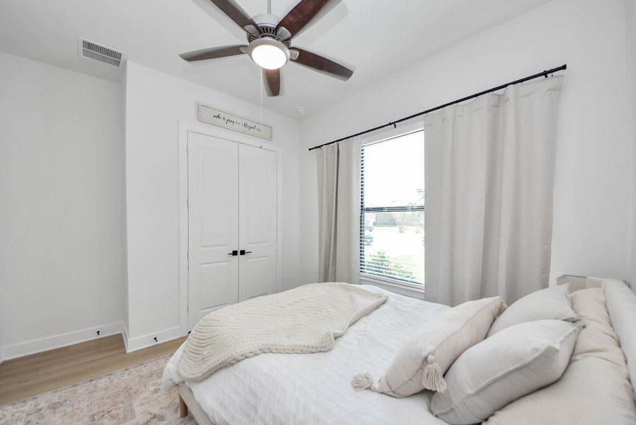 Bright and cozy bedroom featuring a large window with elegant drapes, a comfortable bed, and a ceiling fan for added comfort.
