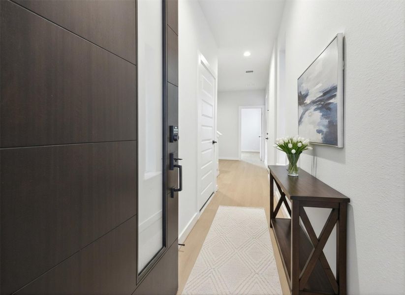 Entryway features a modern aesthetic with LVP light oak–style floors and crisp white trim for a clean, welcoming feel. The open staircase leads to the upper level, and just beyond it, an entry to a guest suite/flex space adds convenience and versatility to the layout. *Virtually staged*