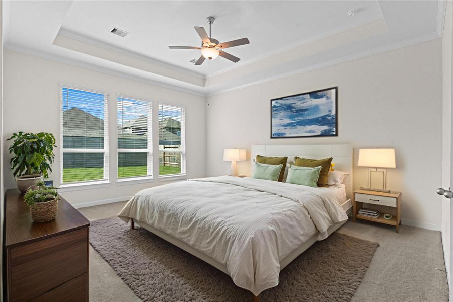 Virtually staged primary suite with tall ceilings, ceiling fan, and wall of windows overlooking the backyard, creating a bright and restful retreat.