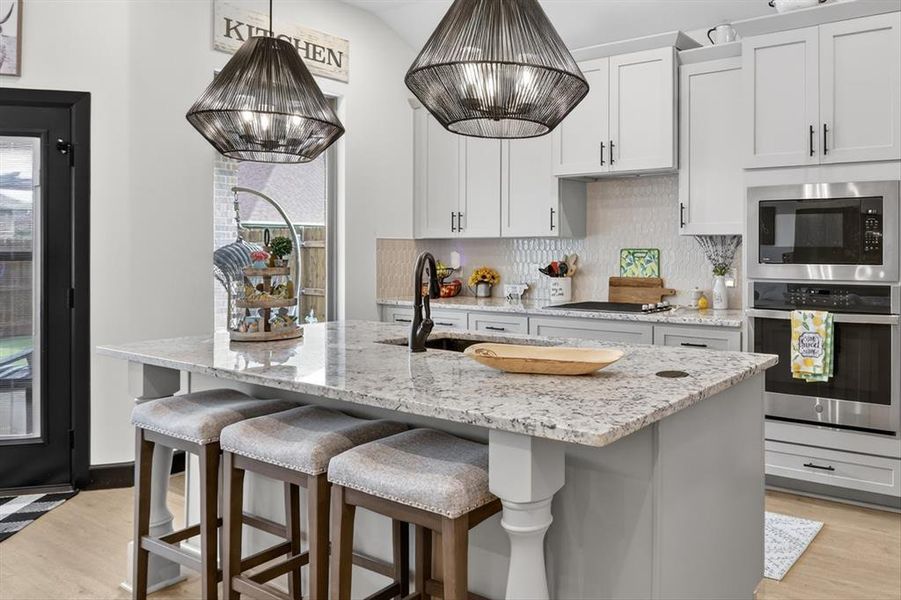 Contemporary kitchen featuring a spacious island with a light-toned countertop, light gray perimeter cabinetry, and stainless steel built-in appliances