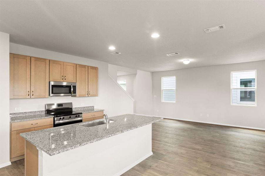 Kitchen featuring appliances with stainless steel finishes, light wood finished floors, an island with sink, light stone counters, and recessed lighting