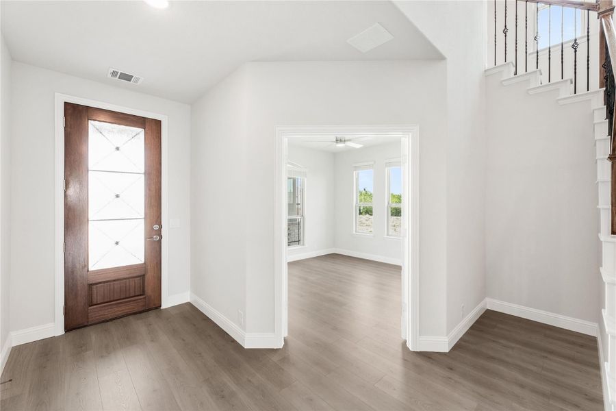 Entryway with wood front door, glass panels, hardwood floors, and staircase with iron balusters