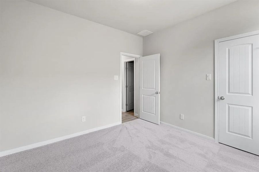 A spacious room offers comfortable carpeted flooring and crisp white doors.