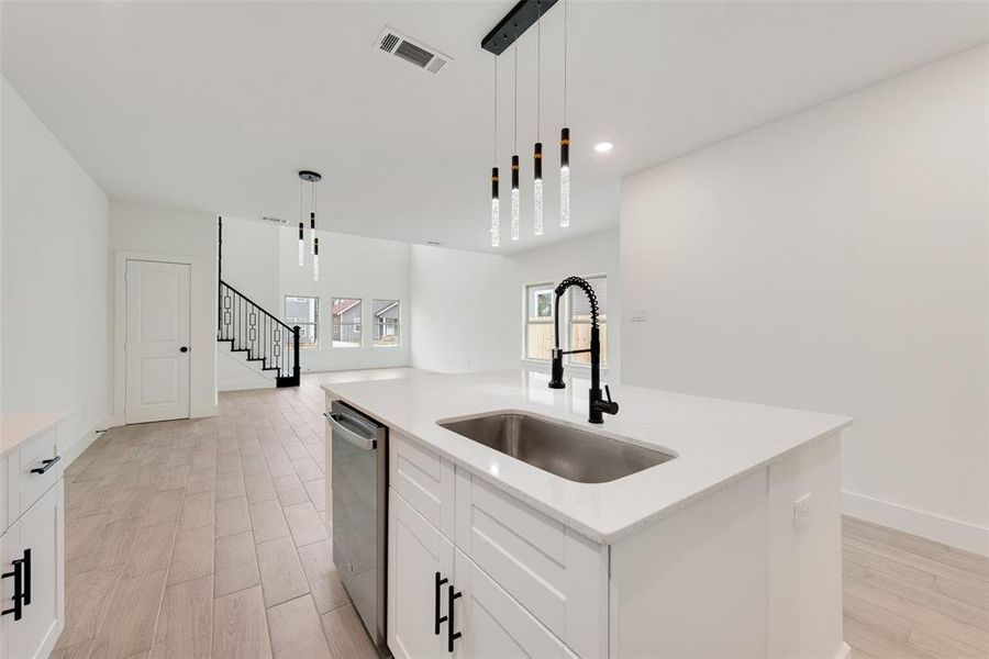 Kitchen with a kitchen island with sink, a sink, white cabinetry, dishwasher, and pendant lighting