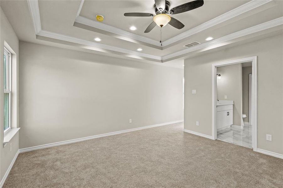 Unfurnished bedroom featuring light colored carpet, ornamental molding, and a tray ceiling