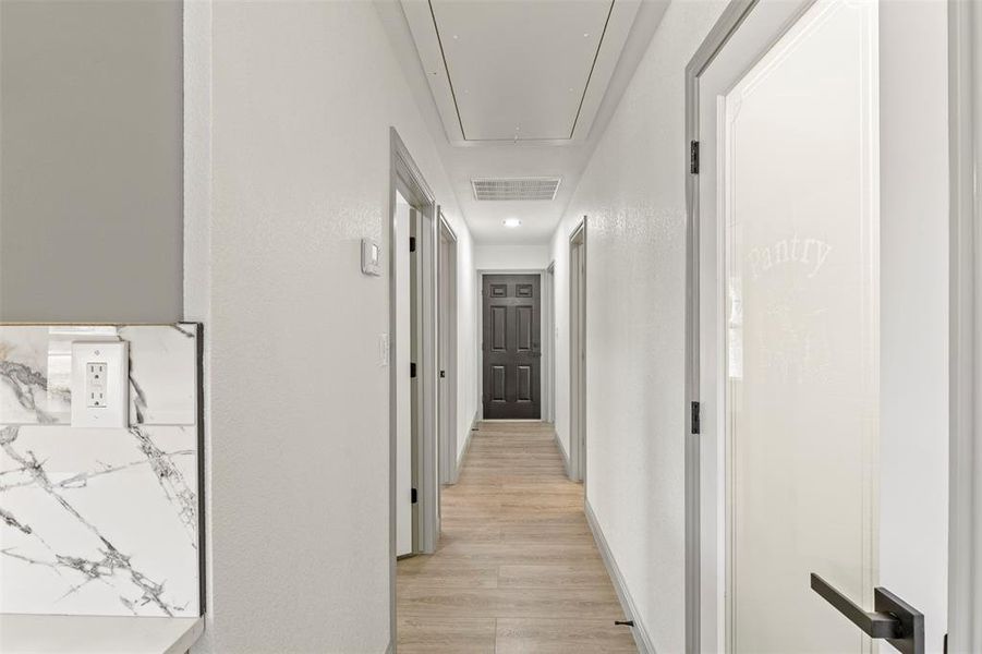 Corridor with light wood-type flooring, a textured wall, and recessed lighting