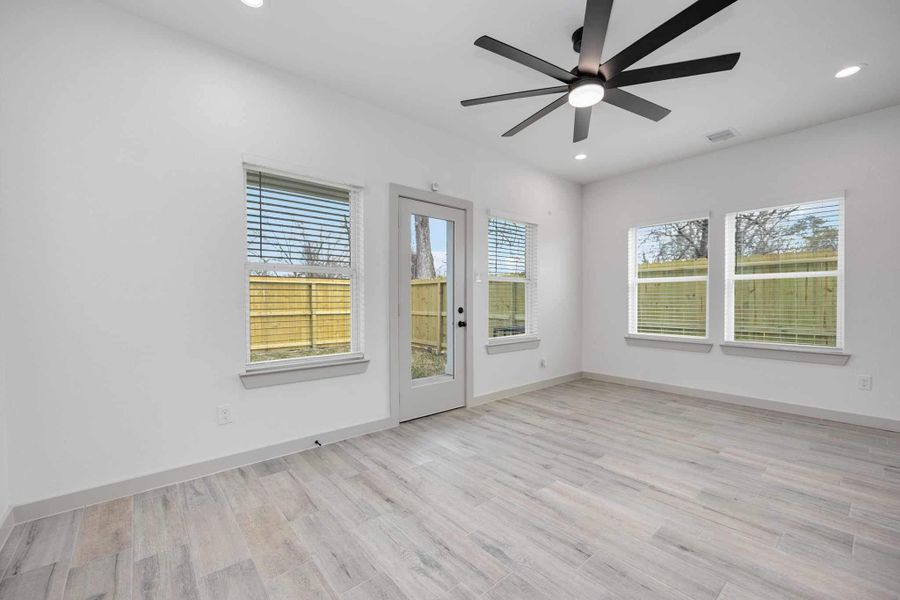 Spacious living room with soaring ceilings, recessed lighting, and a modern ceiling fan. Multiple windows and glass back door provide great natural light and views of the backyard.