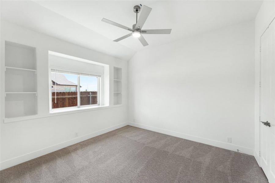 Empty bedroom with vaulted ceiling, ceiling fan, built-in shelves, and carpet flooring