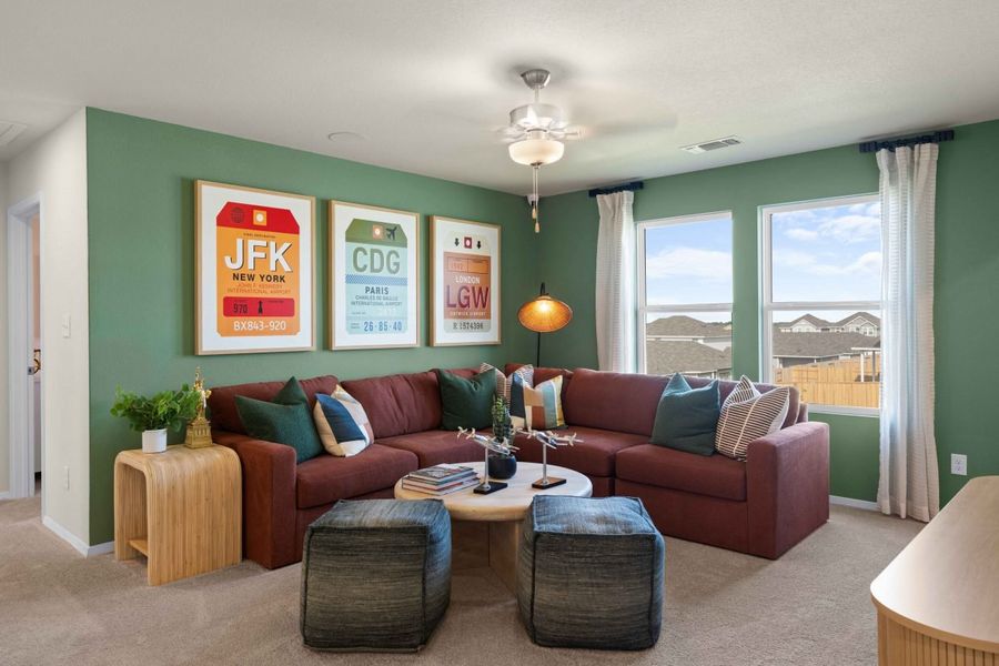 An interior room with windows, brown carpet, green painted walls, a maroon couch, with colorful art and pillows.