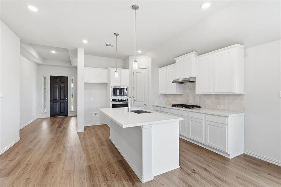 Kitchen featuring white cabinets, a center island with sink, stainless steel appliances, pendant lighting, and light wood-type flooring