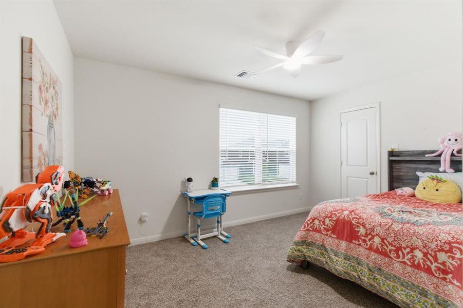 The room features light gray carpet flooring, a ceiling fan with integrated lighting, and a window fitted with blinds