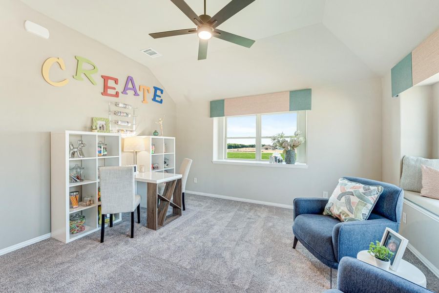 Children's craft room with vaulted ceiling, desk, white shelving unit, and blue seating area on carpet
