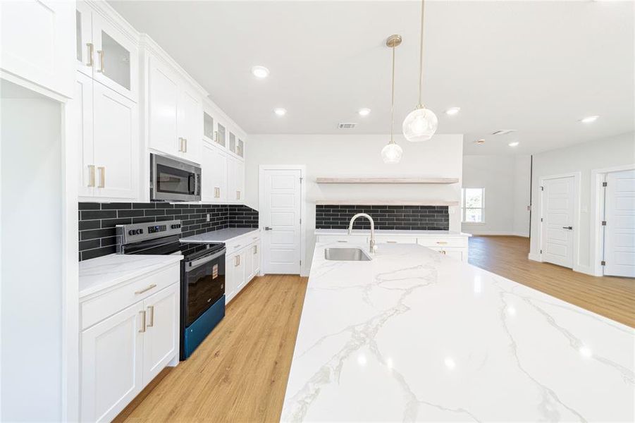 Kitchen with glass insert cabinets, appliances with stainless steel finishes, light wood-type flooring, light stone counters, and recessed lighting Kitchen with glass insert cabinets, appliances with stainless steel finishes, light wood-type flooring, light stone counters, and recessed lighting