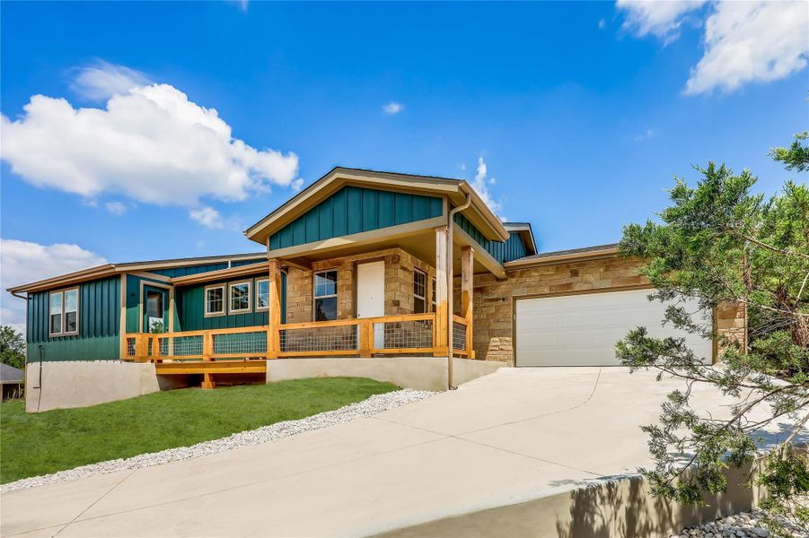 View of front facade featuring board and batten siding, stone siding, a garage, and concrete driveway