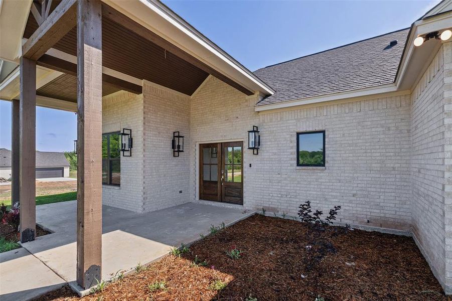 Brick exterior with dark gray shingles, a covered entryway with exposed wood beams, and a wood-finish double entry door featuring glass inserts
