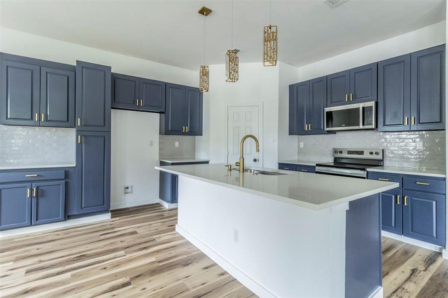 Kitchen featuring stainless steel appliances, backsplash, light countertops, blue cabinetry, and a sink Kitchen featuring stainless steel appliances, backsplash, light countertops, blue cabinetry, and a sink