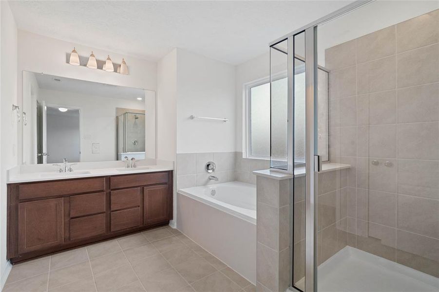 This primary bathroom is definitely move-in ready! Featuring an oversized tub and walk-in shower with tile surround, stained cabinets with light countertops, dual vanities, high ceilings, neutral paint, sleek and modern finishes.