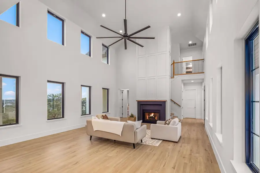 Living area featuring visible vents, stairway, light wood-style flooring, a glass covered fireplace, and baseboards