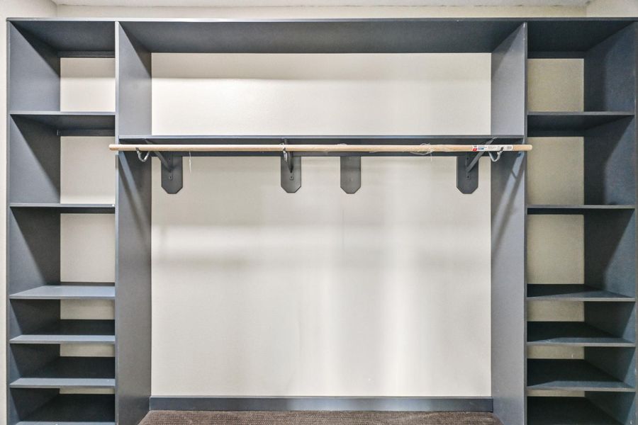 This spacious walk-in closet is thoughtfully designed with custom built-in shelving and abundant storage throughout. Multiple open shelving sections provide the perfect space for shoes, accessories, and organization.