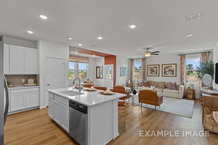 Kitchen with stainless steel dishwasher, ceiling fan, sink, a center island with sink, and white cabinetry