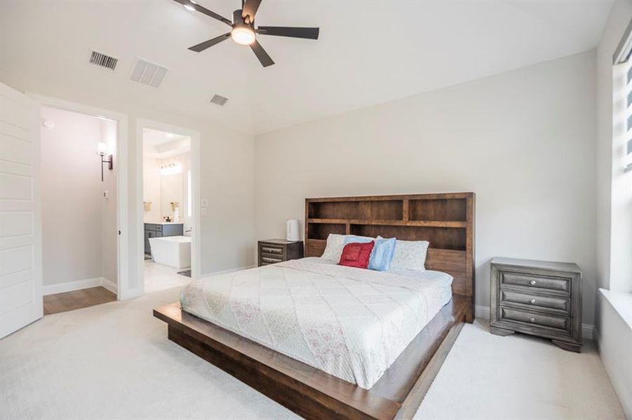 Carpeted bedroom with a ceiling fan, ensuite bath, baseboards, and visible vents