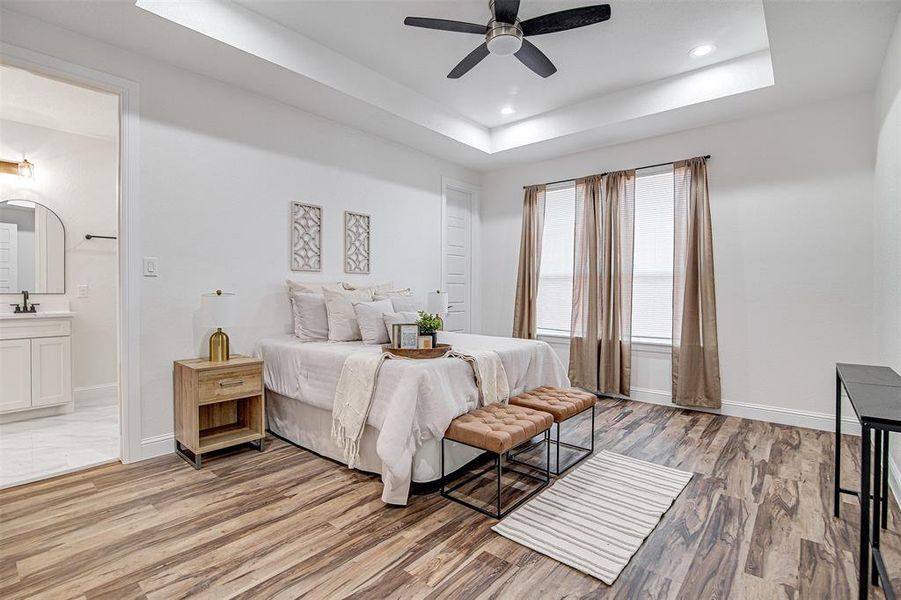 Bedroom with ceiling fan, light wood-type flooring, connected bathroom, and a tray ceiling