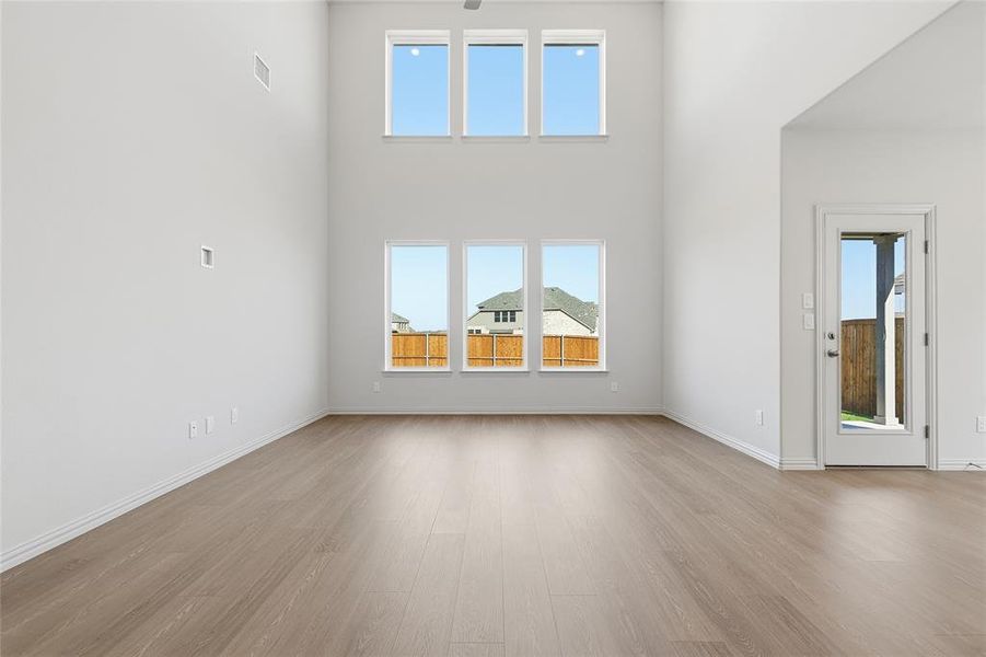 Unfurnished living room featuring healthy amount of natural light, light wood finished floors, and a high ceiling Unfurnished living room featuring healthy amount of natural light, light wood finished floors, and a high ceiling
