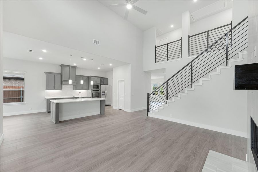 Open-concept living area with two-story ceiling, gray kitchen island, and staircase with metal railing