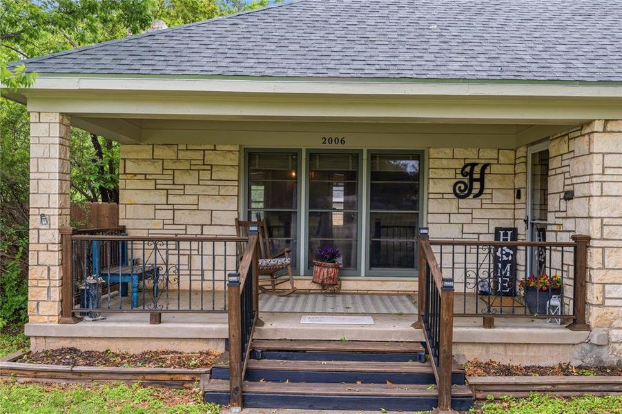 Stone facade home featuring a covered front porch, dark wood newel posts, and metal porch railing Stone facade home featuring a covered front porch, dark wood newel posts, and metal porch railing